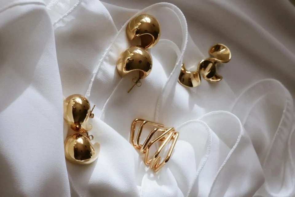 Gold dome earrings and minimalist ring on soft white fabric with elegant styling