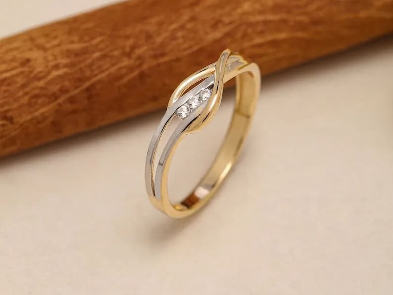 A delicate gold and silver ring with a twisted design and three small diamonds.
