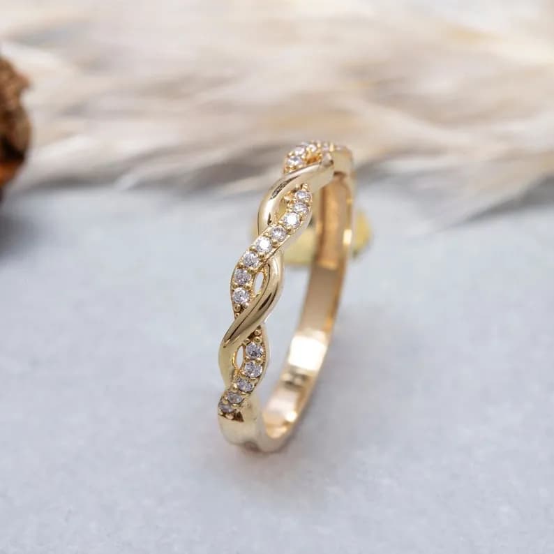 A delicate gold band ring with a twisted design and small clear stones set along the band.