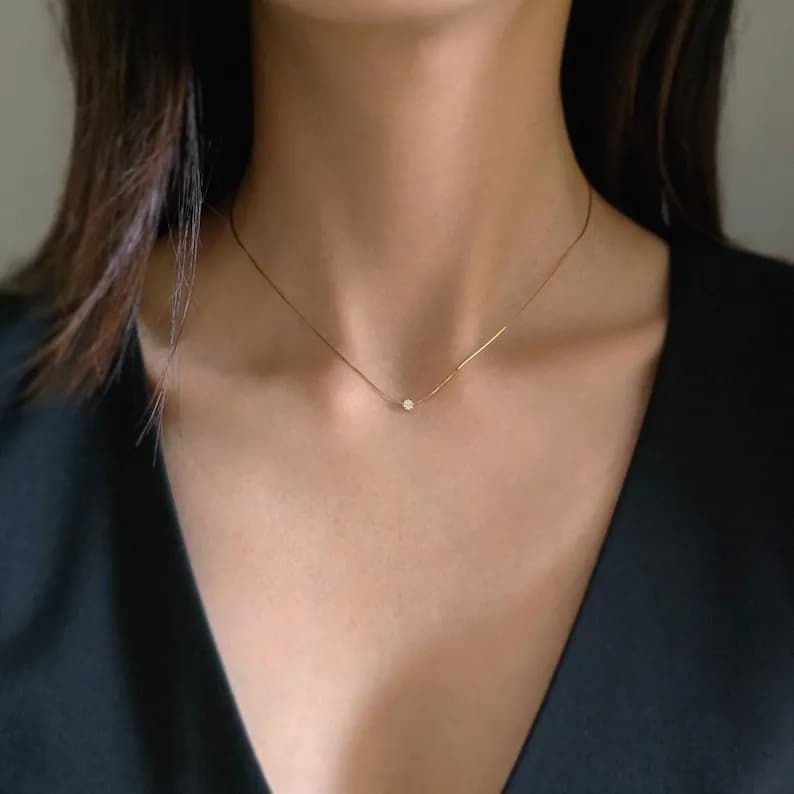 Delicate gold necklace featuring a small, round, clear gemstone pendant on a thin chain.
