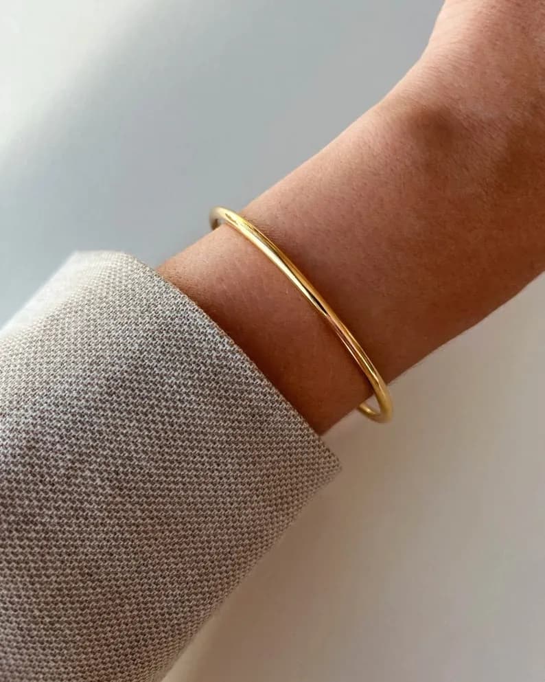 A simple gold bangle bracelet on a person's wrist.