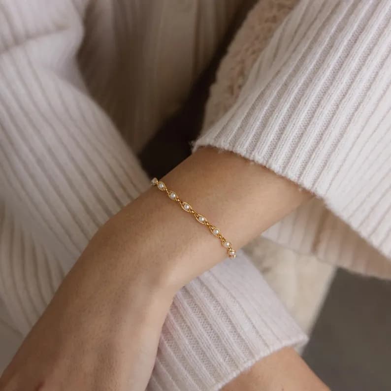 Gold chain bracelet with small white pearls on a person's wrist.