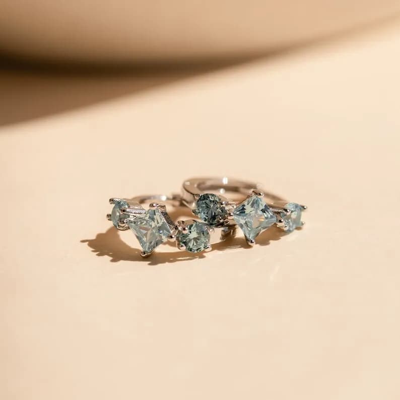 A pair of silver hoop earrings with clusters of light blue gemstones.