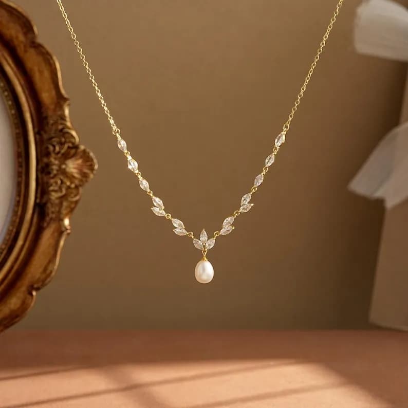 Delicate gold-toned necklace featuring a leaf-like design with clear, sparkling accents and a teardrop-shaped pearl pendant.