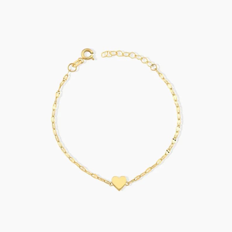 Delicate gold bracelet featuring a small heart charm, displayed on a white background.