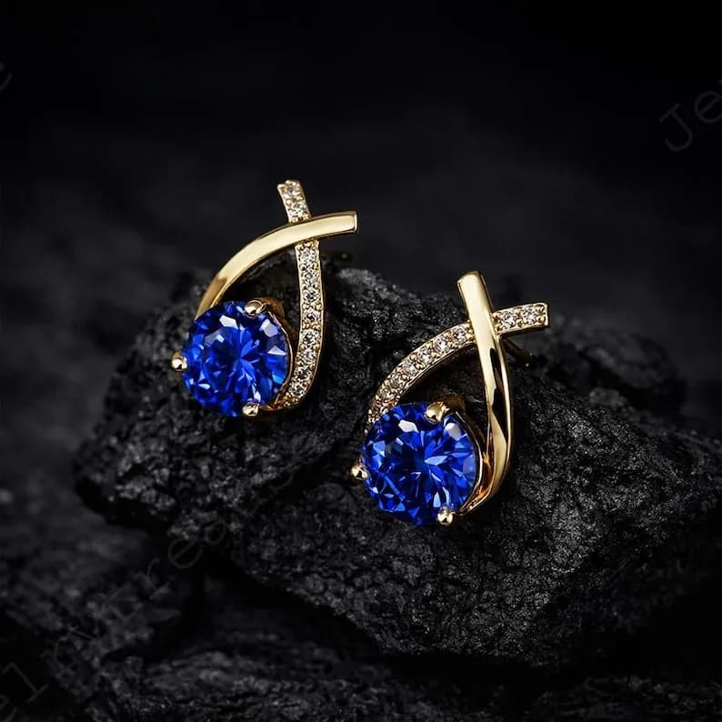 Gold stud earrings featuring large round deep blue sapphires with clear accent stones.